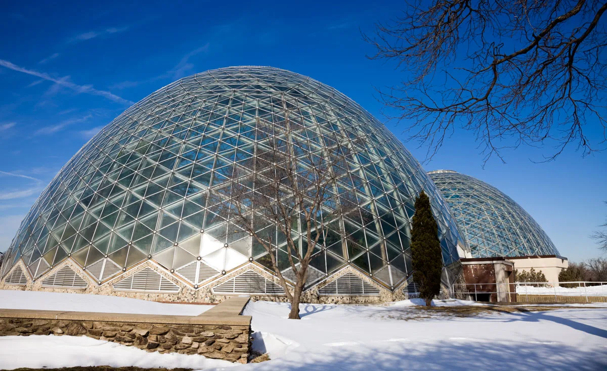 Large glass domes that house botanic gardens surrunded by snow on a sunny day in Milwaukee. 