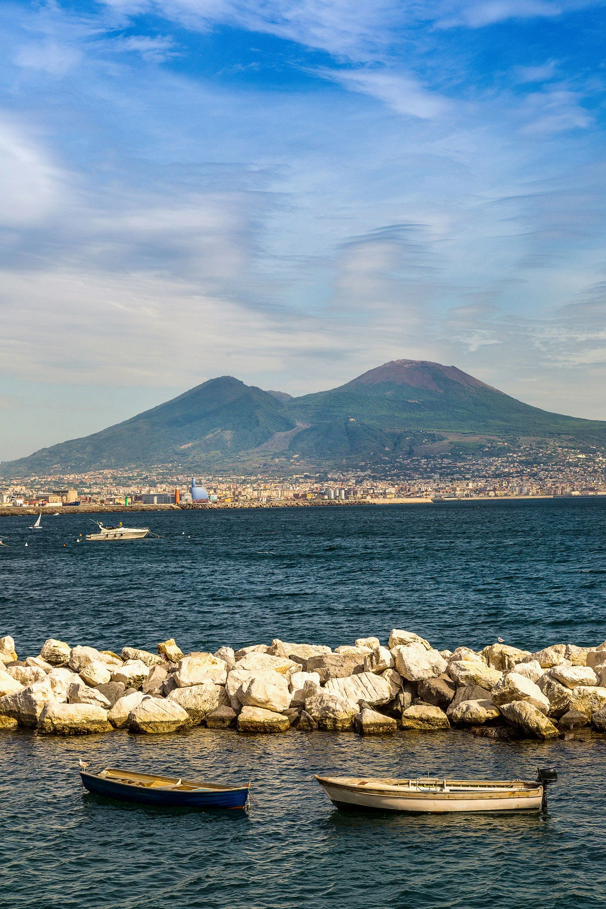 Small row boats moored in a breakwater in Naples harbour with Mt Vesuvius in the background. 