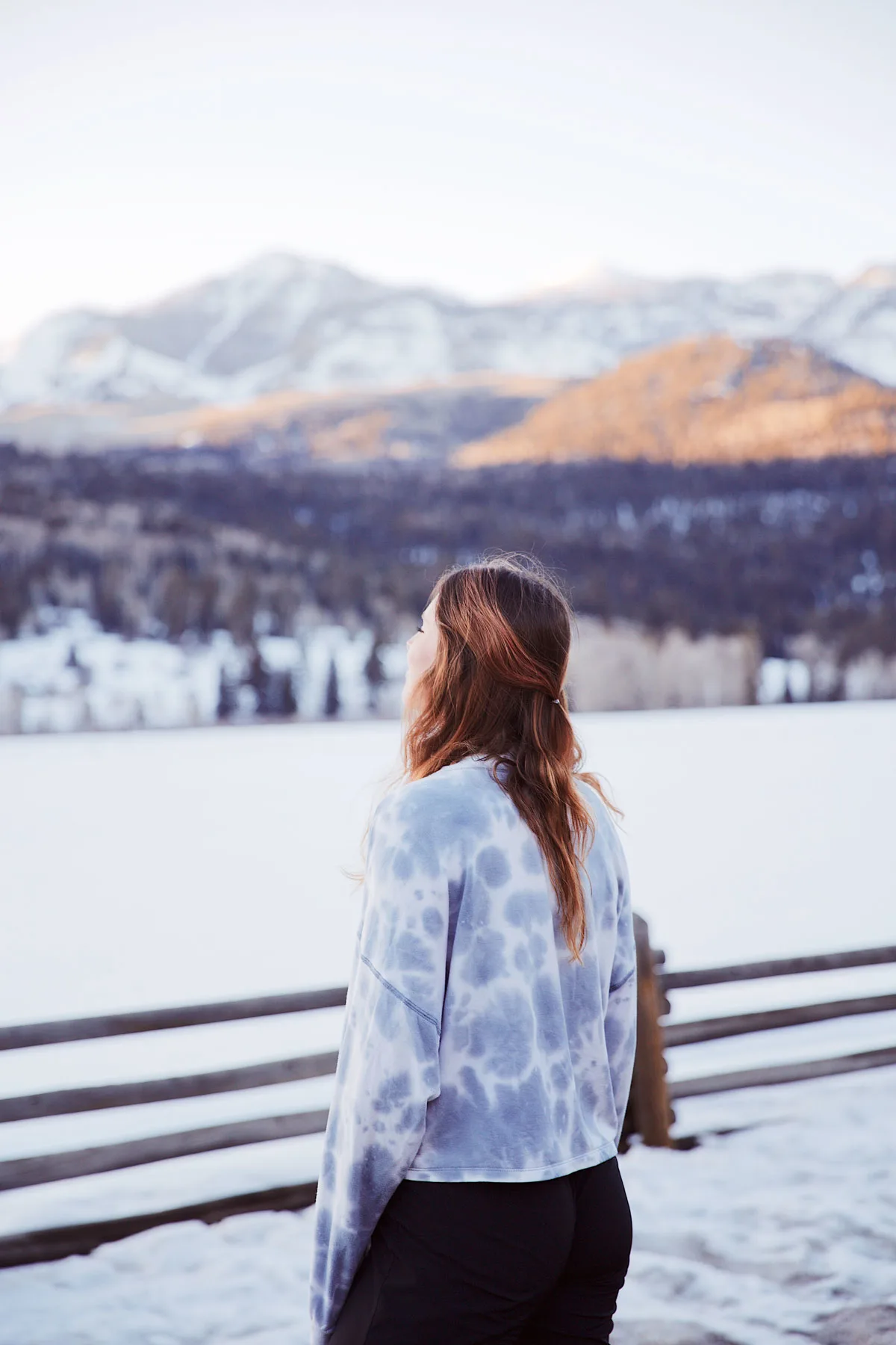 Young girl looking out over a snowy field with mountains in the distance. 