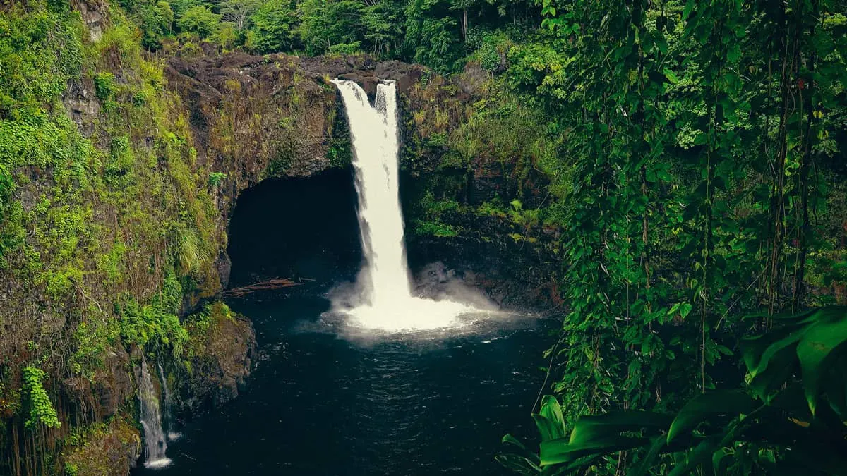 Rainbow Falls Waterfall and swimming hole surrounded by lush jungle vegetation on Big Island Hawaii. 