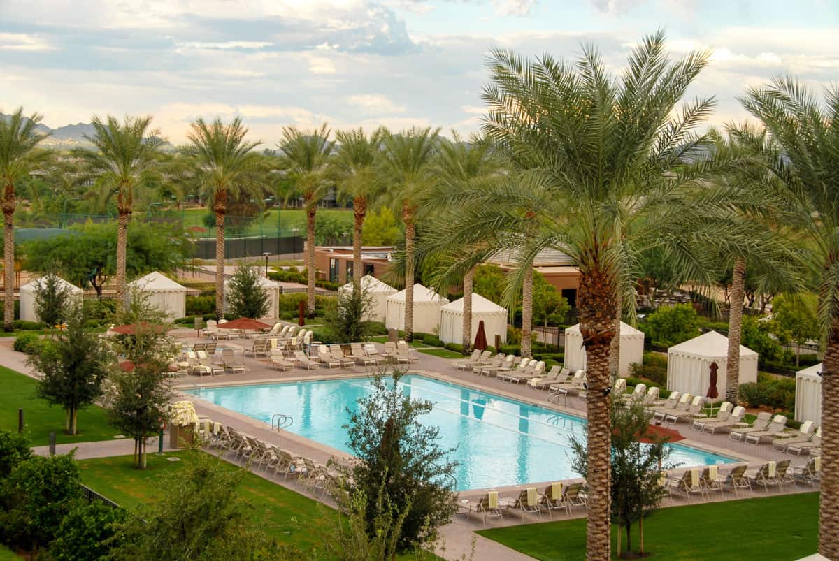 A large luxury pool in the centre of a resort in Scottsdale Arizona in winter surrounded by palm trees and green grass. 