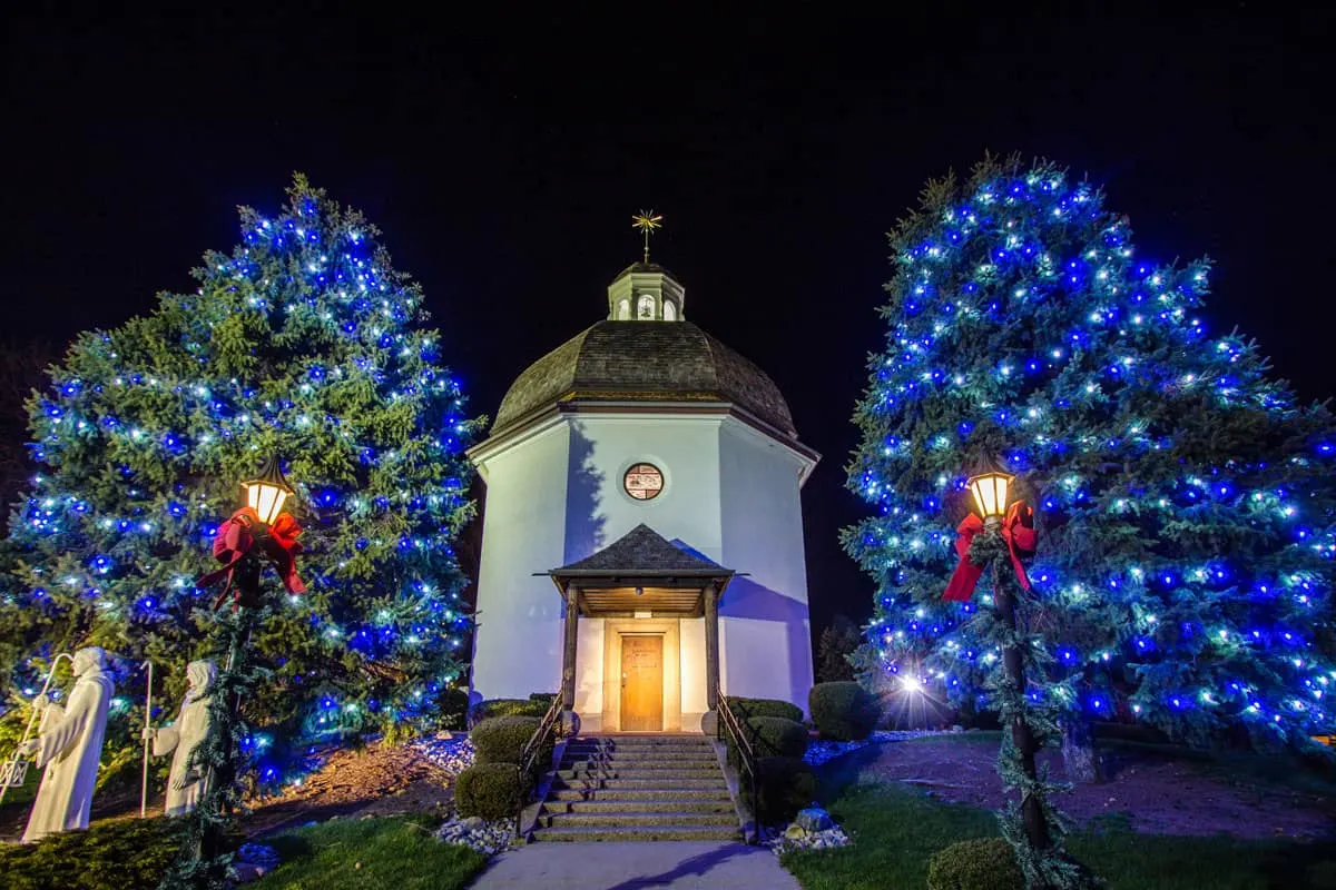 Trees covered in blue christmas lights next to the Silent night replica building in Frankenmuth Michigan. 