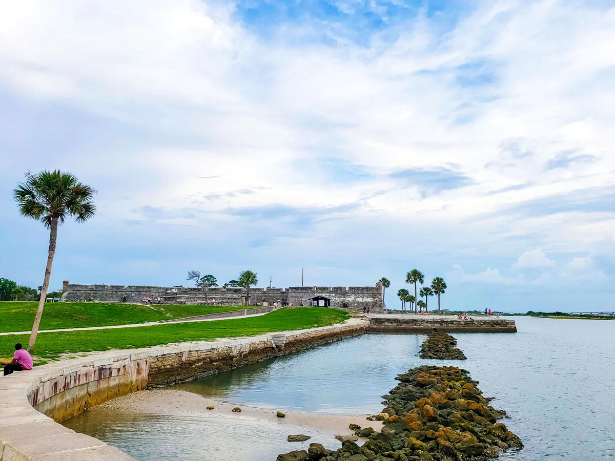 Canal views in St Augustine flanked by green grass and palm trees with an old Spanish fort on the canal banks.