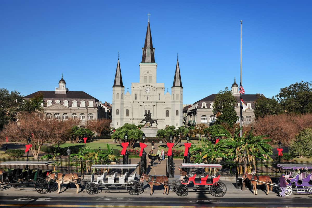 HOrse and cart tours parke in front of the Saint Louis Cathedral in the French Quarter of New Orleans. It is a sunny day. 