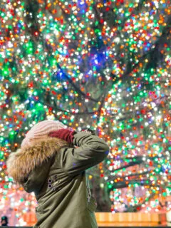 Girl in winter clothing looking up at the colourful lights of an enourmous Christmas tree at the Rockefeller Center in NYC.