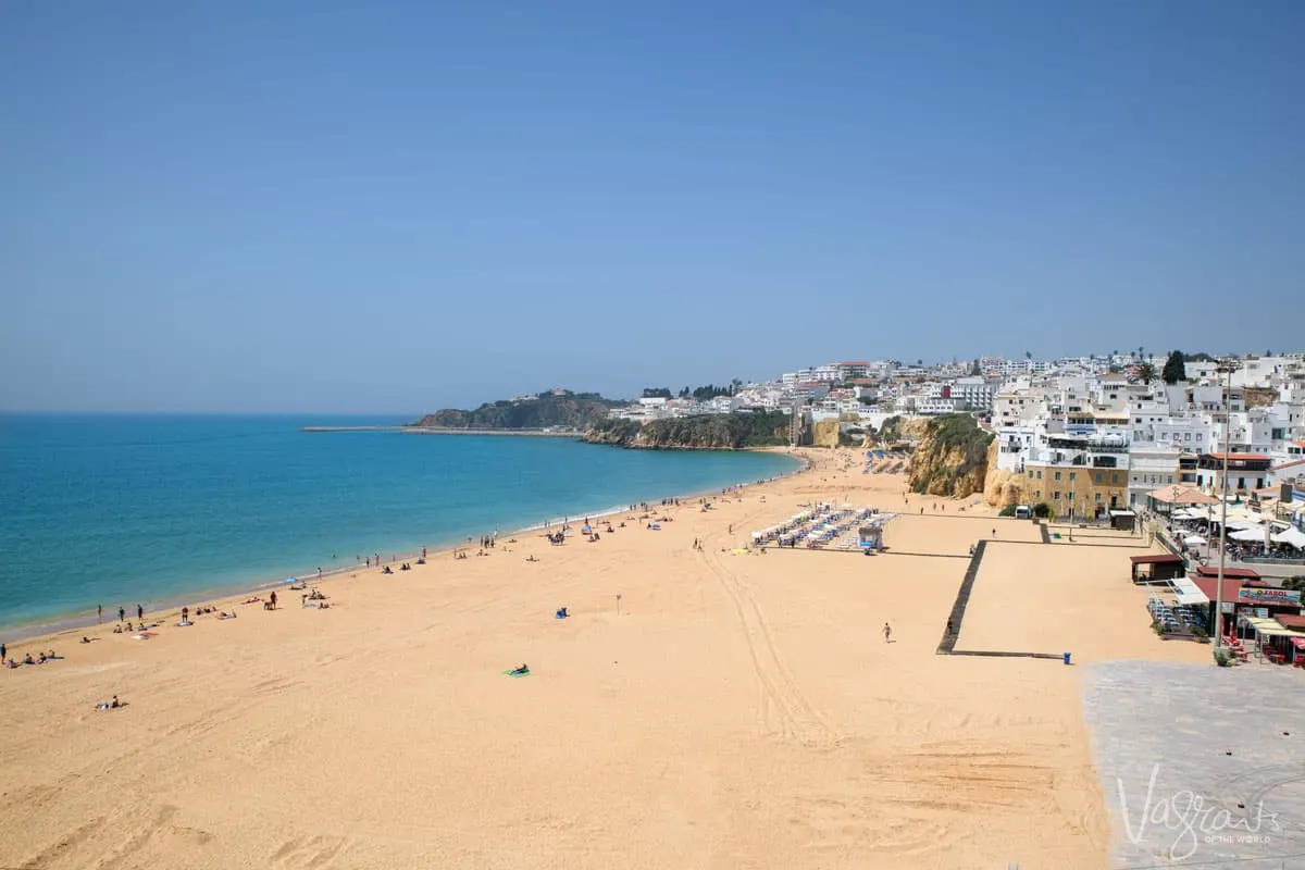 Long expanse of golden sand and calm blue ocean on the beach of Albufeira Portugal. The old town of Albufeir extends along the cliff over looking the beach. 