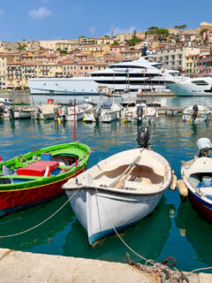 Brightly painted fishing boats and large luxurious yachts are moored in the harbor of Portoferraio on Elba Island. The colorful historical buildings and restaurants line the waterfront.