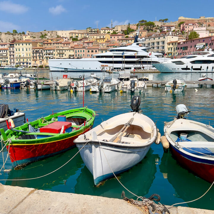 Brightly painted fishing boats and large luxurious yachts are moored in the harbor of Portoferraio on Elba Island. The colorful historical buildings and restaurants line the waterfront.