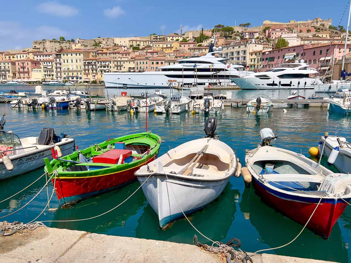 Brightly painted fishing boats and large luxurious yachts are moored in the harbor of Portoferraio on Elba Island. The colorful historical buildings and restaurants line the waterfront. 