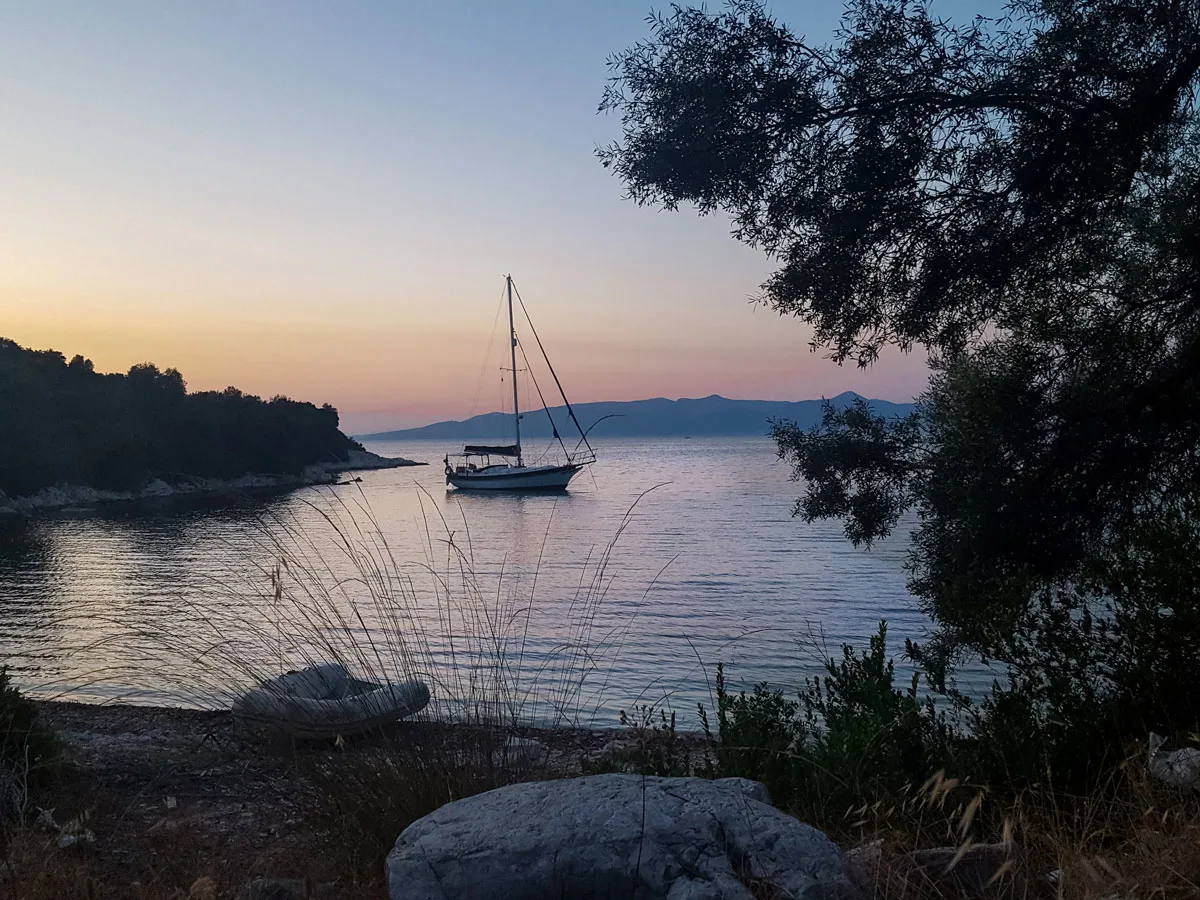 A single yacht moored in a quiet bay at dusk. The sky has hues of pink.