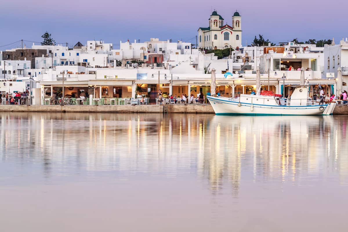 A boat moored in front a waterfront tavernas at dusk on Paros Island. The lights reflect in the water.