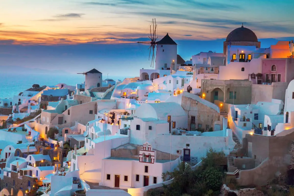 The whitewashed village of Oia glowing gold and blue above the Santorini caldera at dusk.