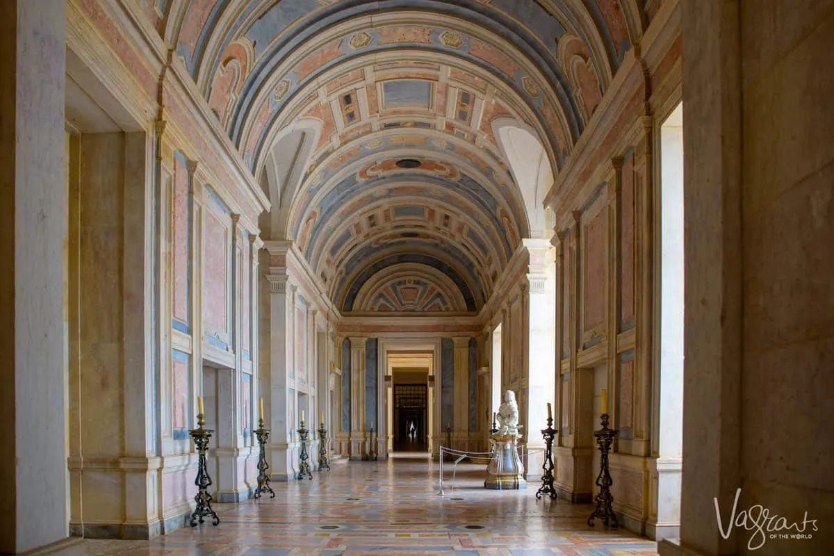 A large, opulent, arched hallway with coloured mosaics and tiles in the National Palace of Mafra in Portugal. 