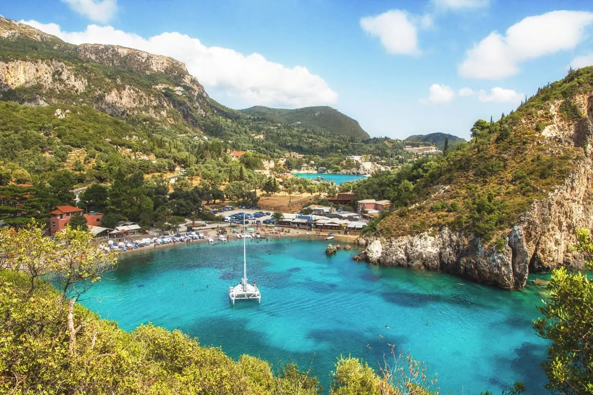 A yacht is moored in the middle of a turquoise blue bay surrounded by green hills. 