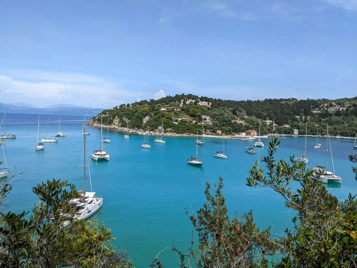 Boats moored in a clear blue bay surrounded by lush green islands in Greece.