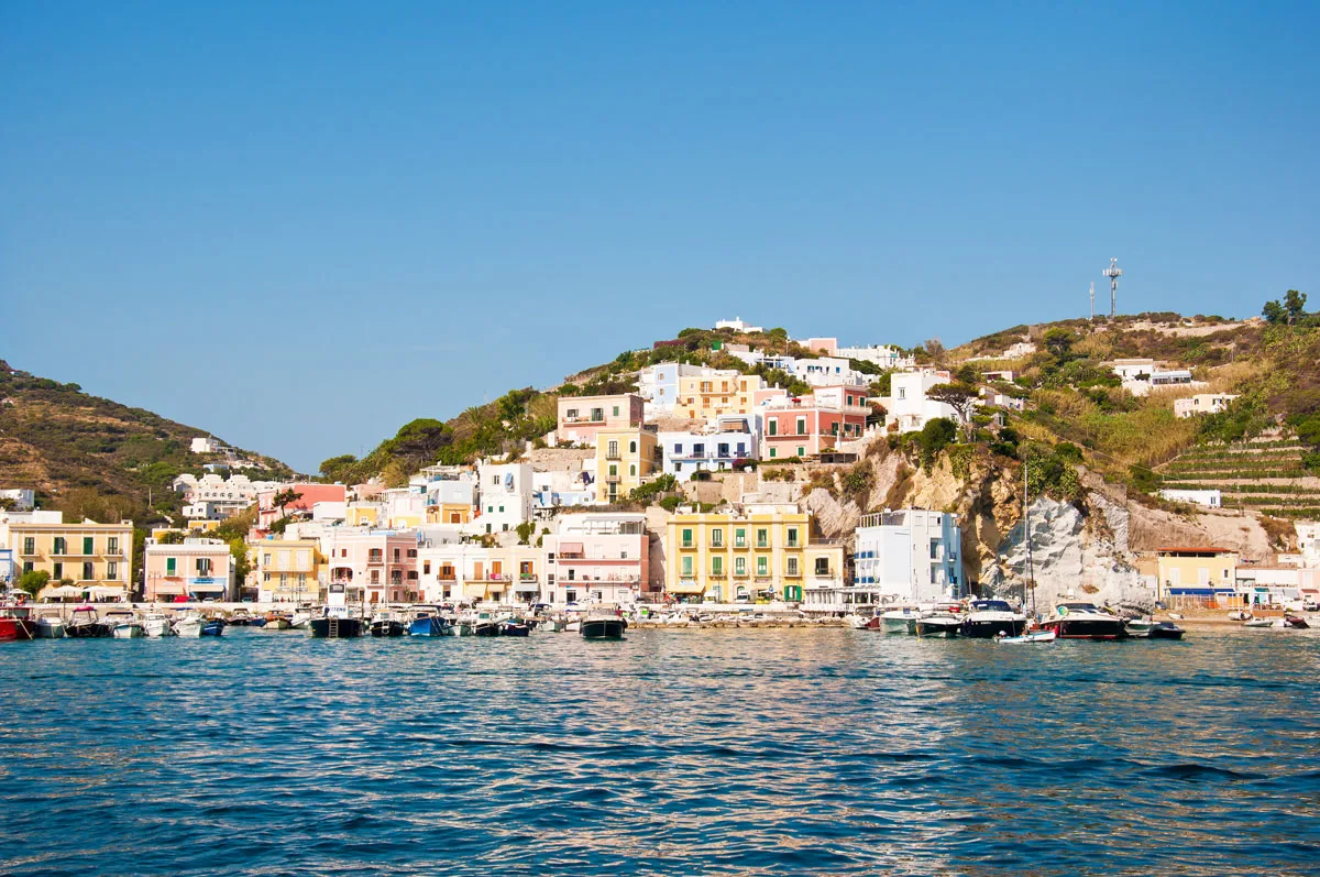 Colourful buildings scatterered over Ponza Island in Italy overlooking boats moored in a blue bay. 