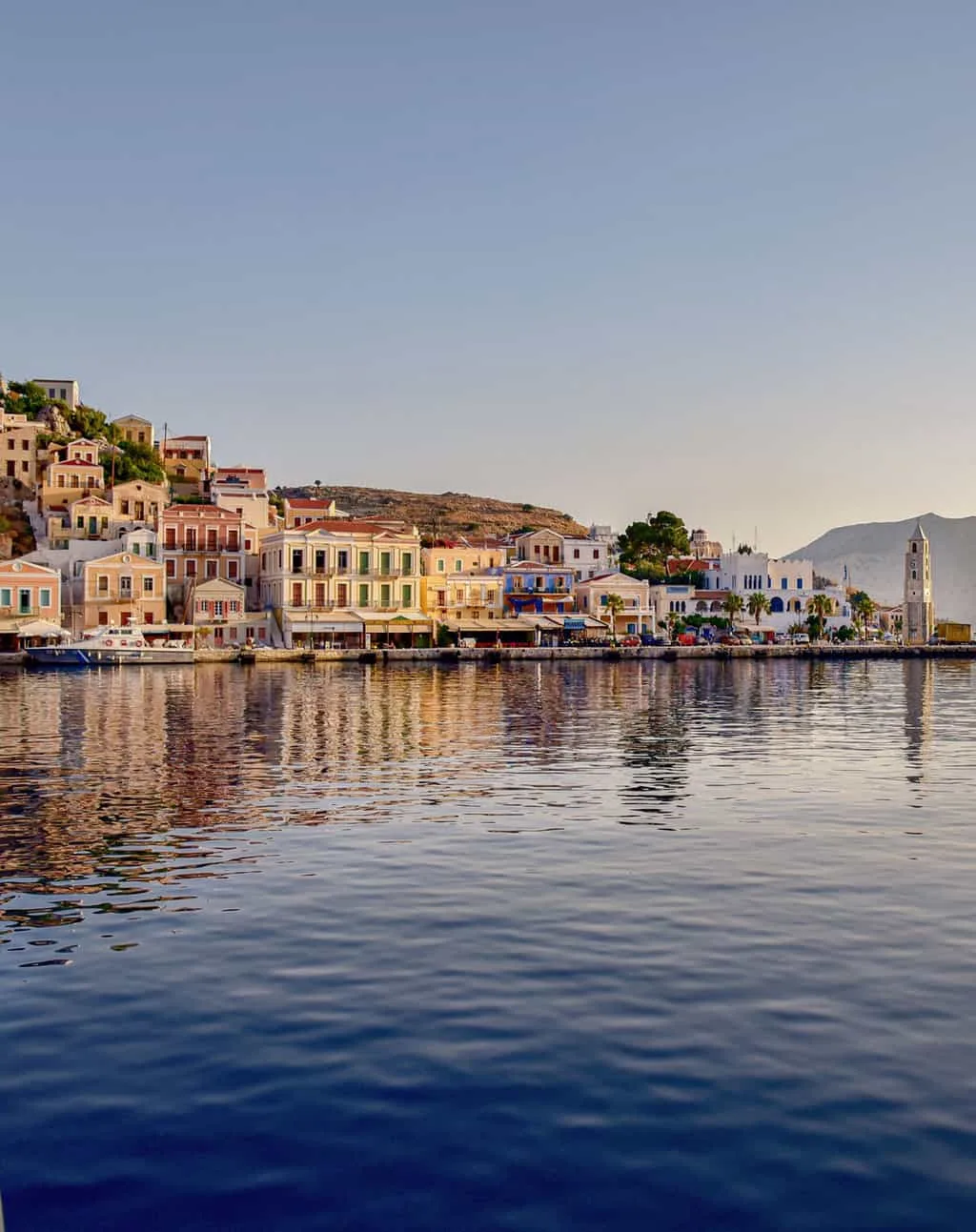 Colourful buldings climb the hill along the waterfront in the main town of Symi Island in Greece. The houses reflect in the water in the low light of dusk. 