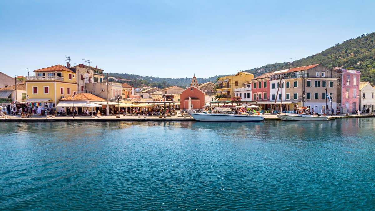 A colorful greek town lines the bay with restuarnts along the waterfront and boats moored. 
