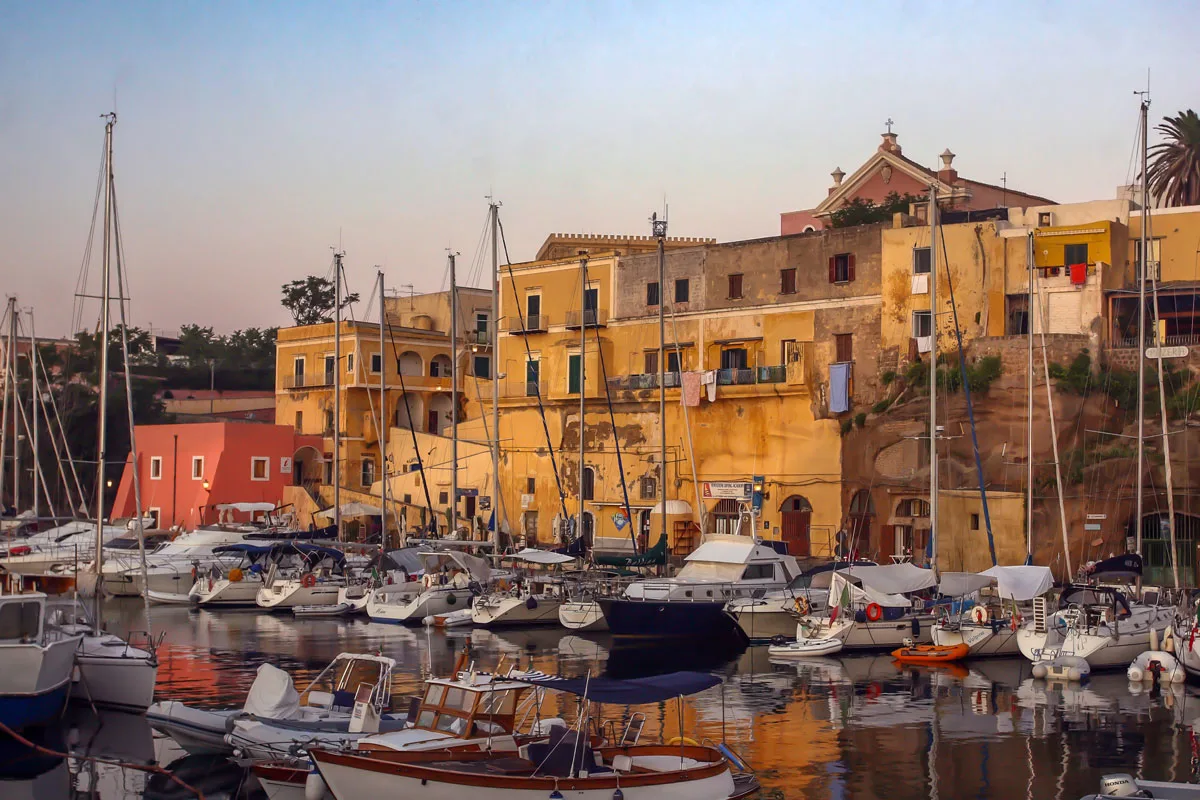 Classic yellow buildings overlooking a small marina at dusk on the Italian island of Ventotene. 