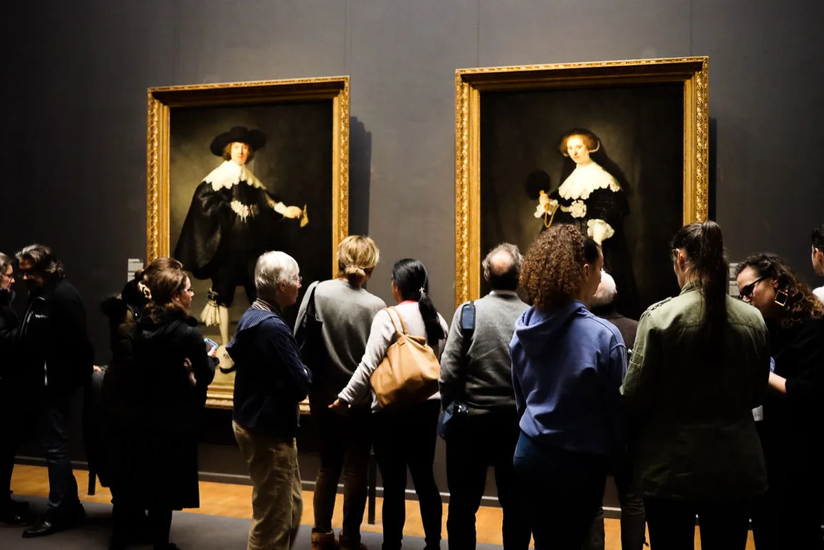 People in an art gallery looking at famous Rembrandt paintings. 