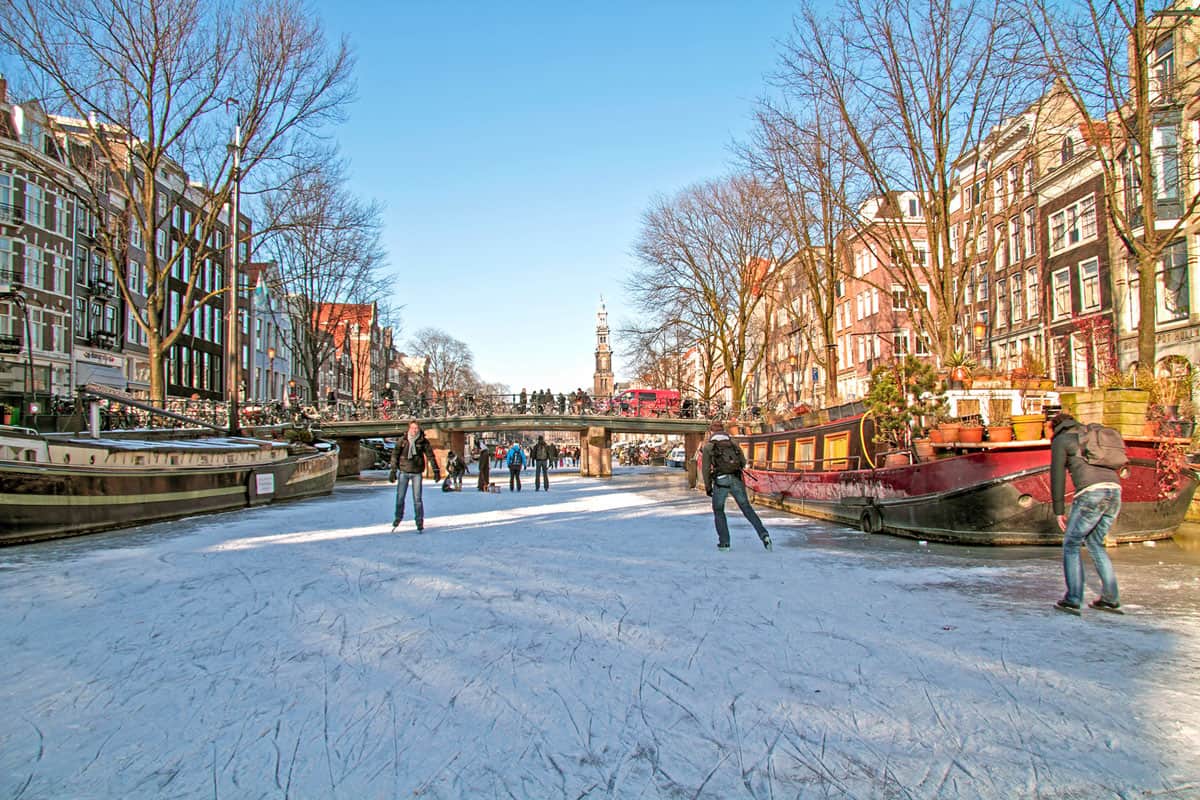 People ice skating on the frozen canals in Amsterdam next to the canal barges. 