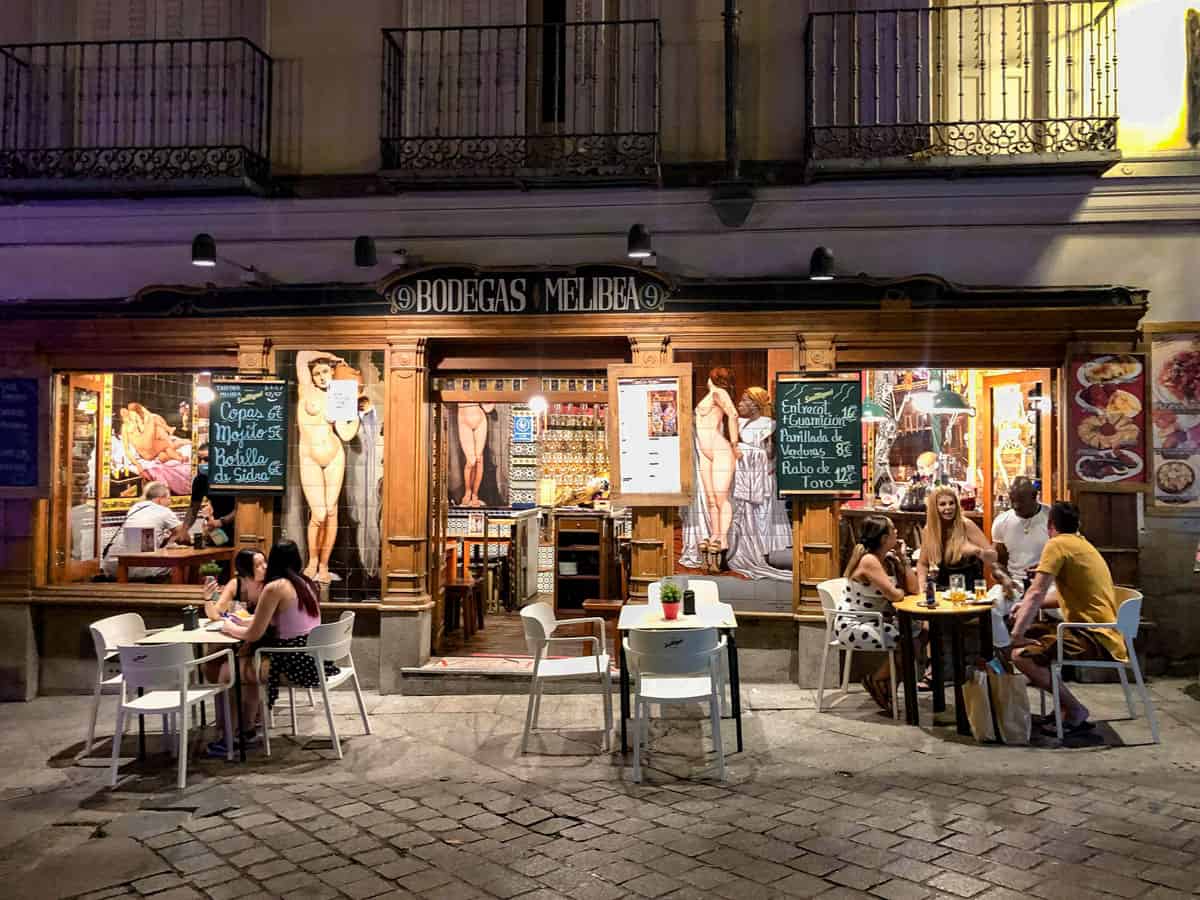People eating out the front of a typical tapas restaurant at night in Madrid.  