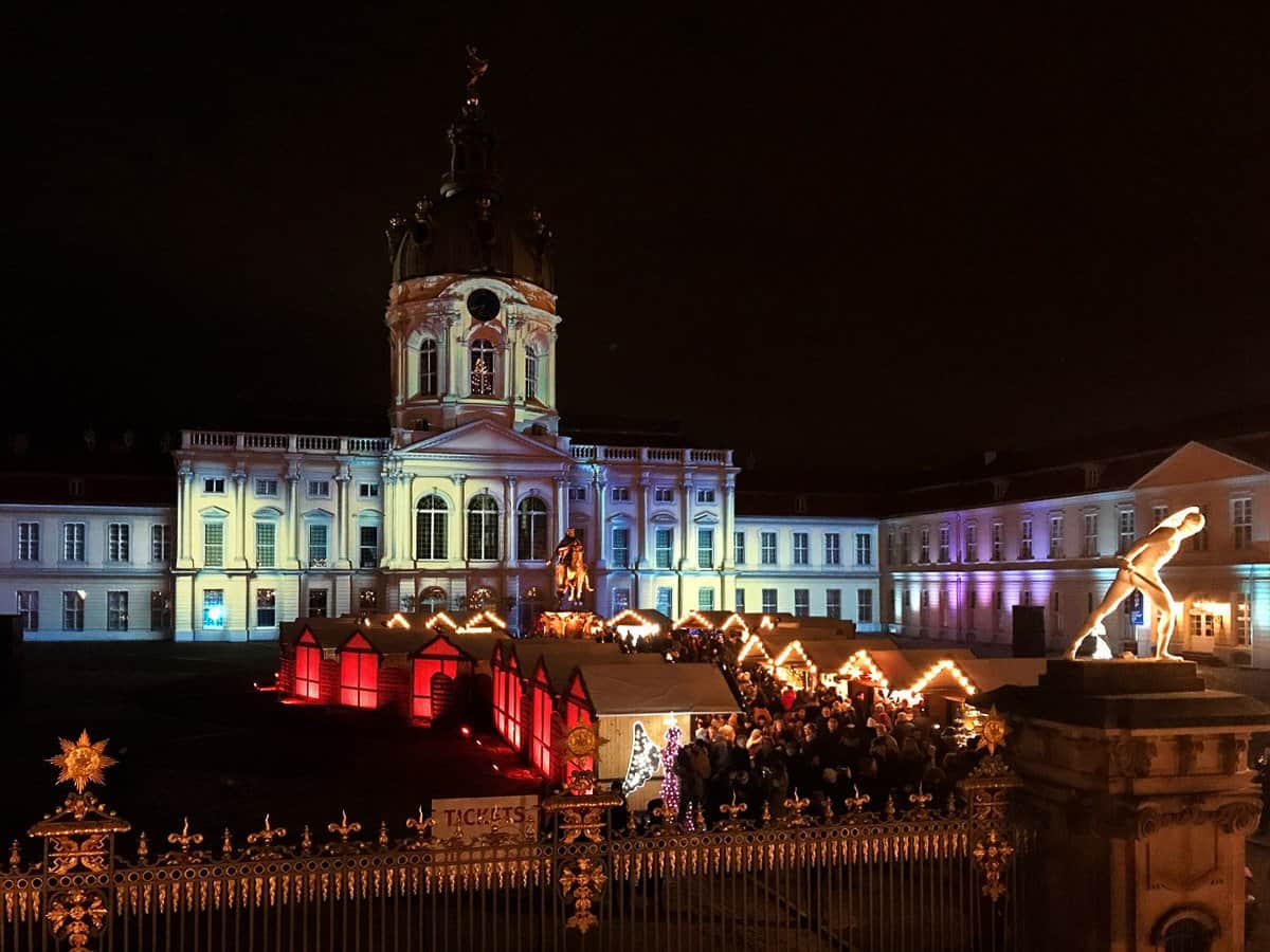 Christmas markets at night in front of a beautifully lit historical building in Berlin. 