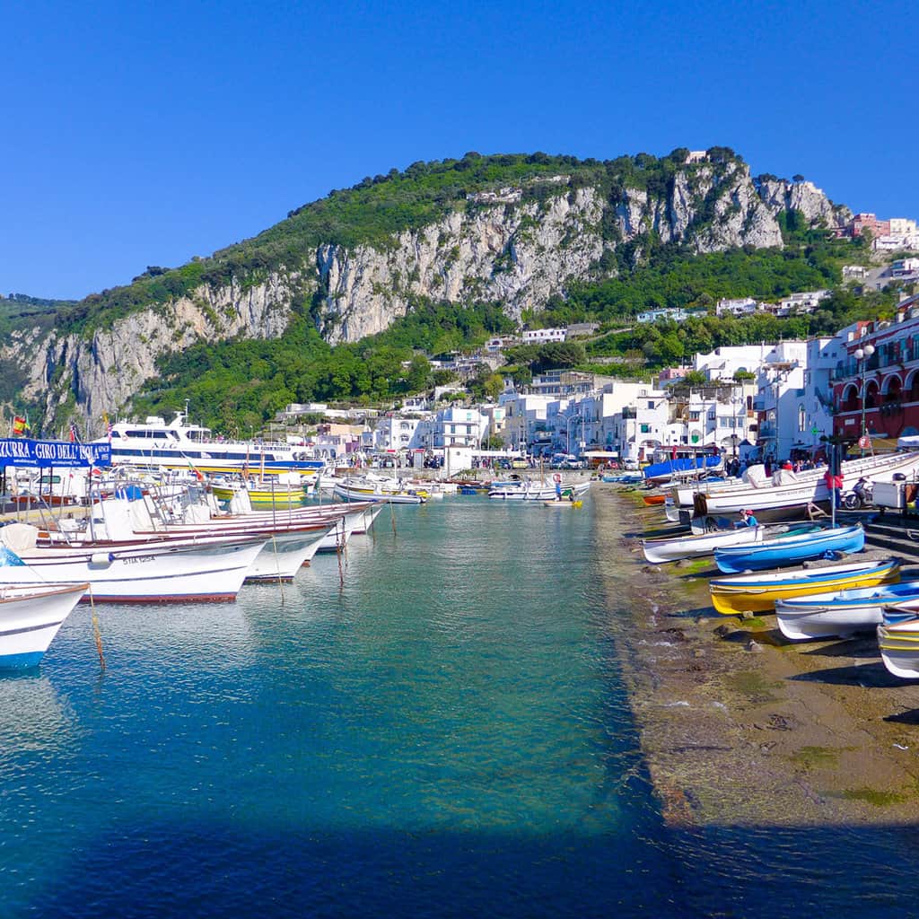 Colourful fishing boats in neat rows on the banks of a harbour on Capri Island.