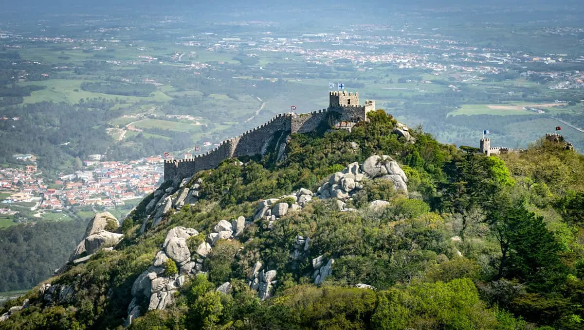 A historical Moorish castle traces the top of a mountain overlooking the town of Sintra in Portugal.