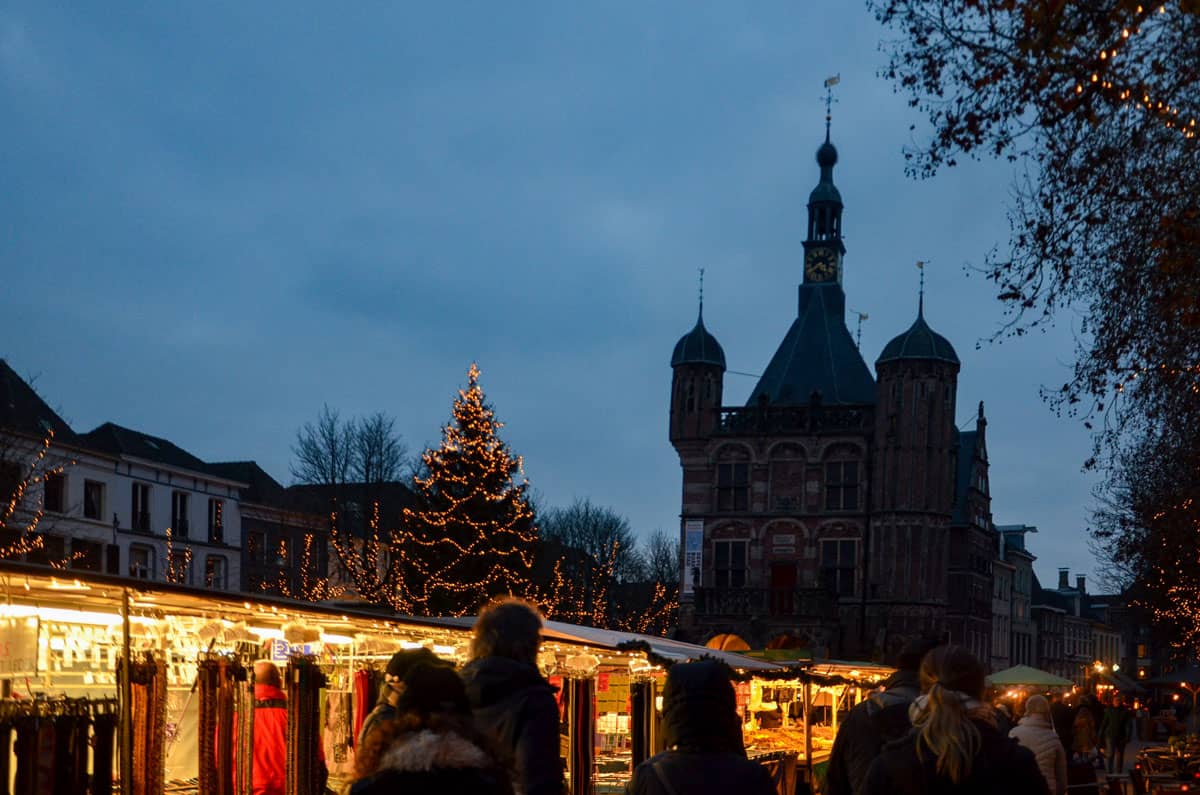 Christmas markets at night with the silhouette of a double spired church in the distance. 