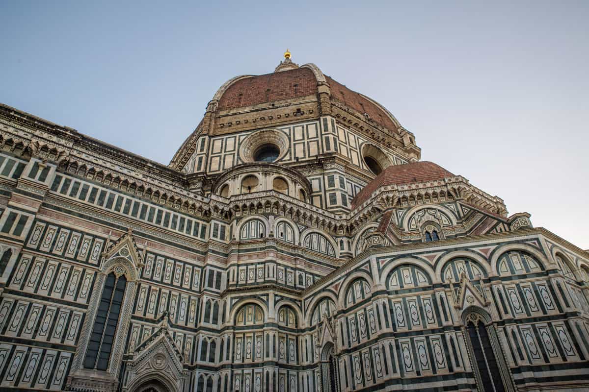 Looking up past the green and white marbled exterior of the Florence cathedral to the large red tiled dome. 