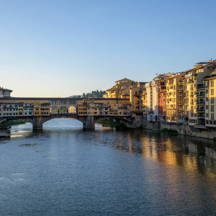 The Arno River in Florence at sunrise with the famous Ponte Vechio Bridge in the distance.