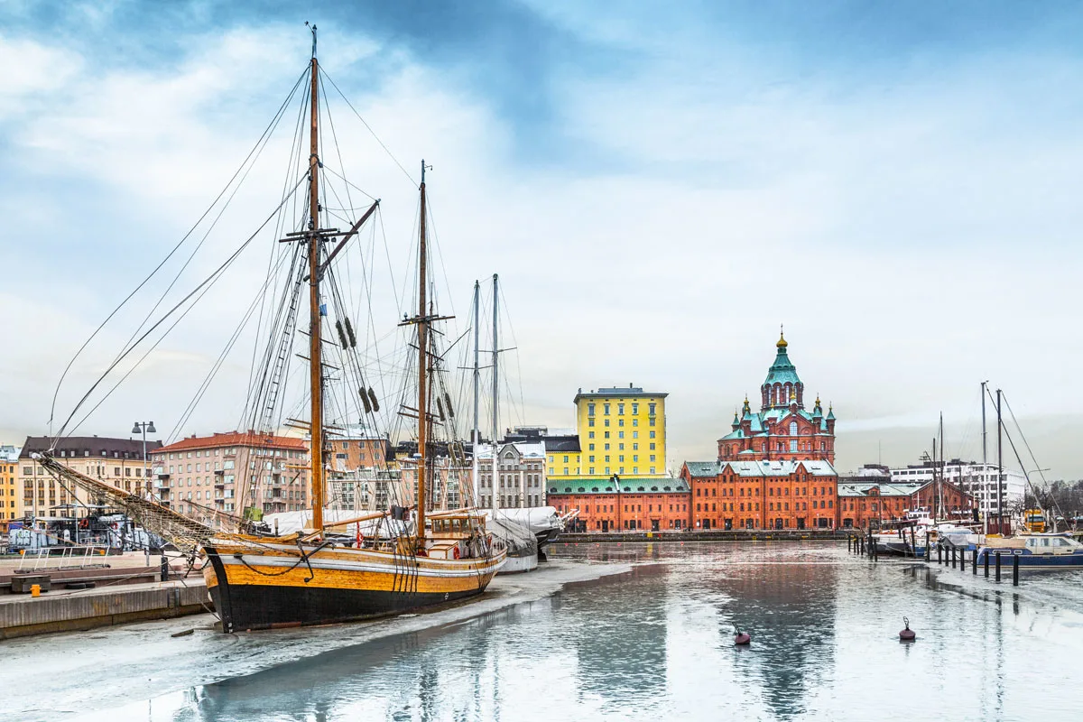 A traditional wooden boat moored in Helsinki harbor district with Uspenski cathedral in the distance during winter in Finland. 