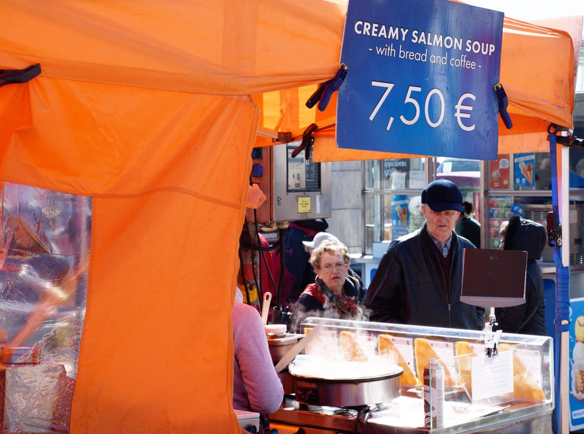 Old man and lady waiting at a market stall in Helsinki that serves hot, creamy salmon soup and coffee as advertsied on the market stall sign. 