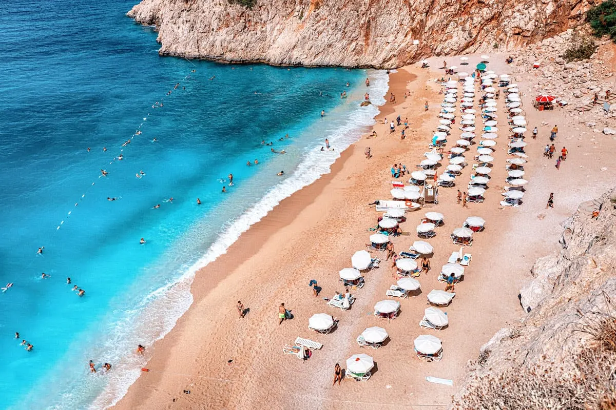 Umbrellas in neat rows on a yellow sand beach with incredibly beautiful turquoise water at Kaputas beach in Turkey. 