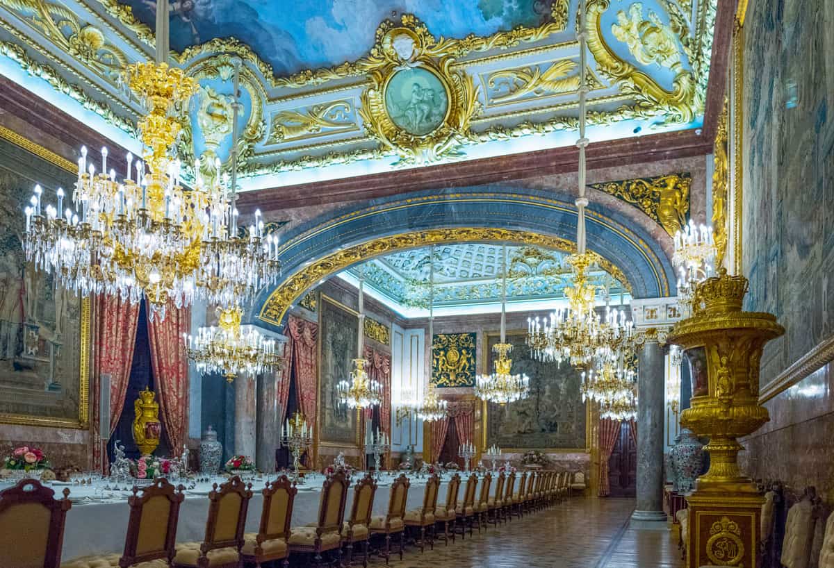 The banguette hall in the Madrid Royal palace with chandeliers and a long table set for dinner. 