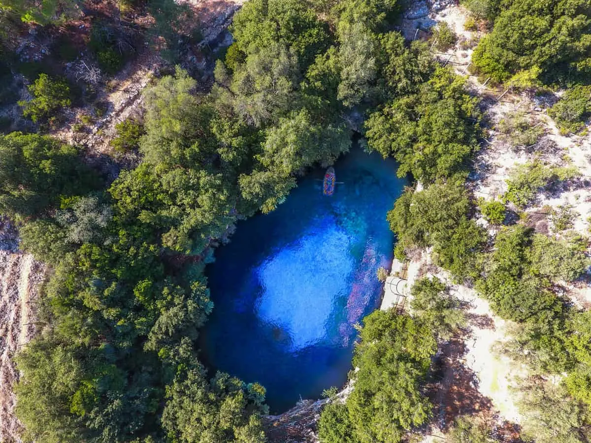 Aerial view of a blue water lake sourrounded by trees. There is a small rowboat in the Lake.