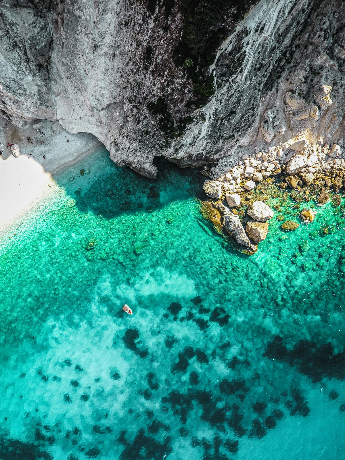 Aerial view of a yacht in clear water near a white beach and steep cliffs.