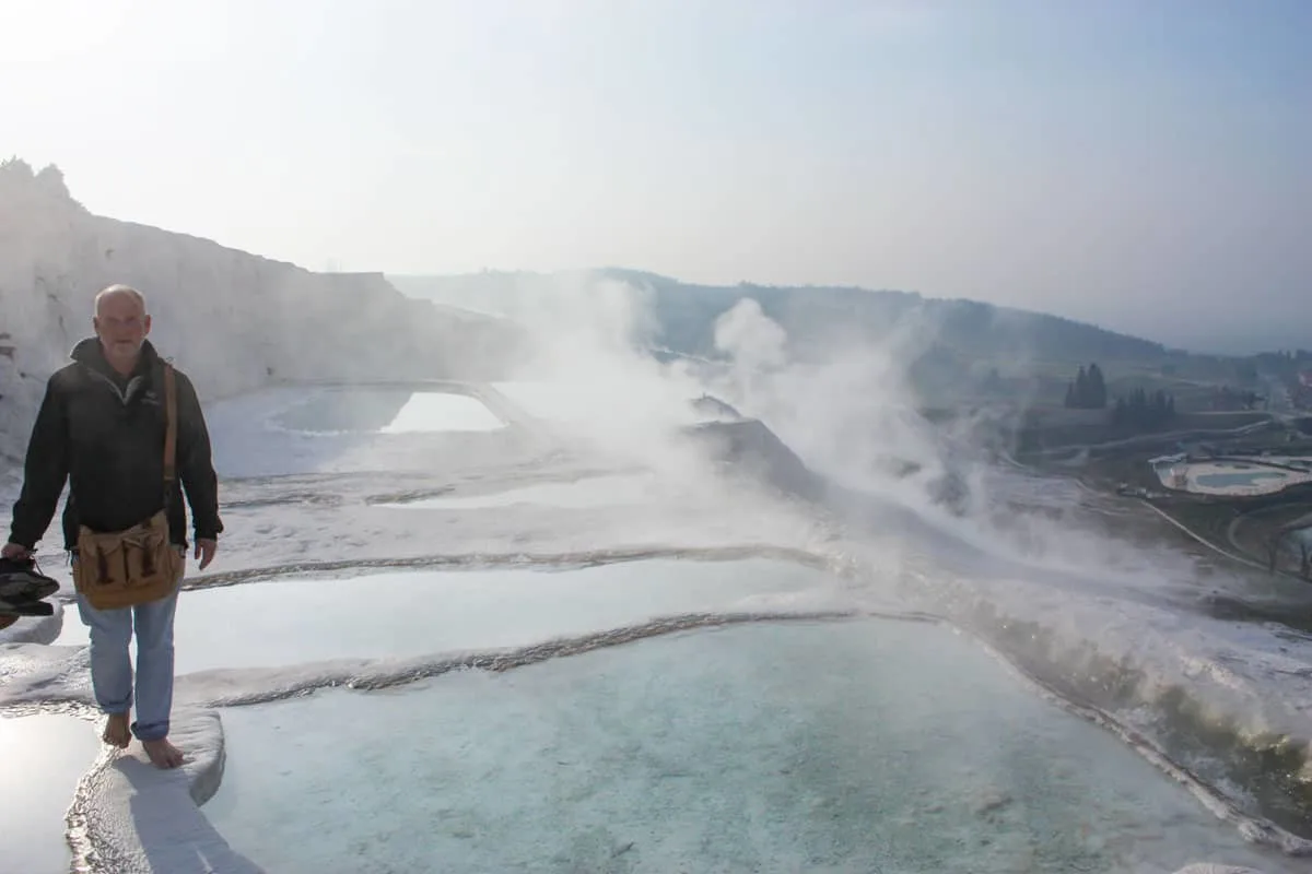 A man walks barefoot through steam over the white travetine deposits that cover the natural thermal spas in Pamukkale in Turkey. 