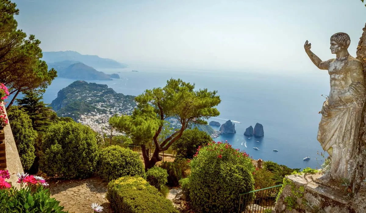 Views over the blue bay from a tranquil garden with roman statue in the garden.