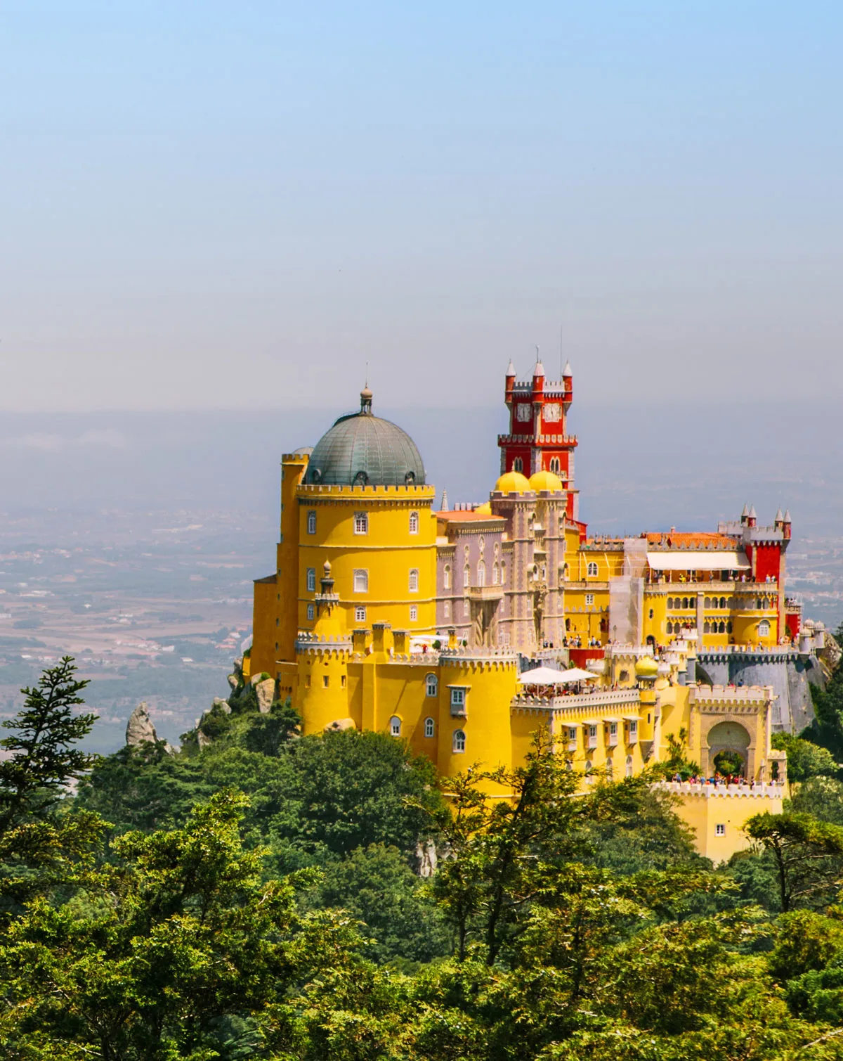 The brightly coloured fairytale style Pena Palace emerges from the green mountain top in Sintra Portugal.
