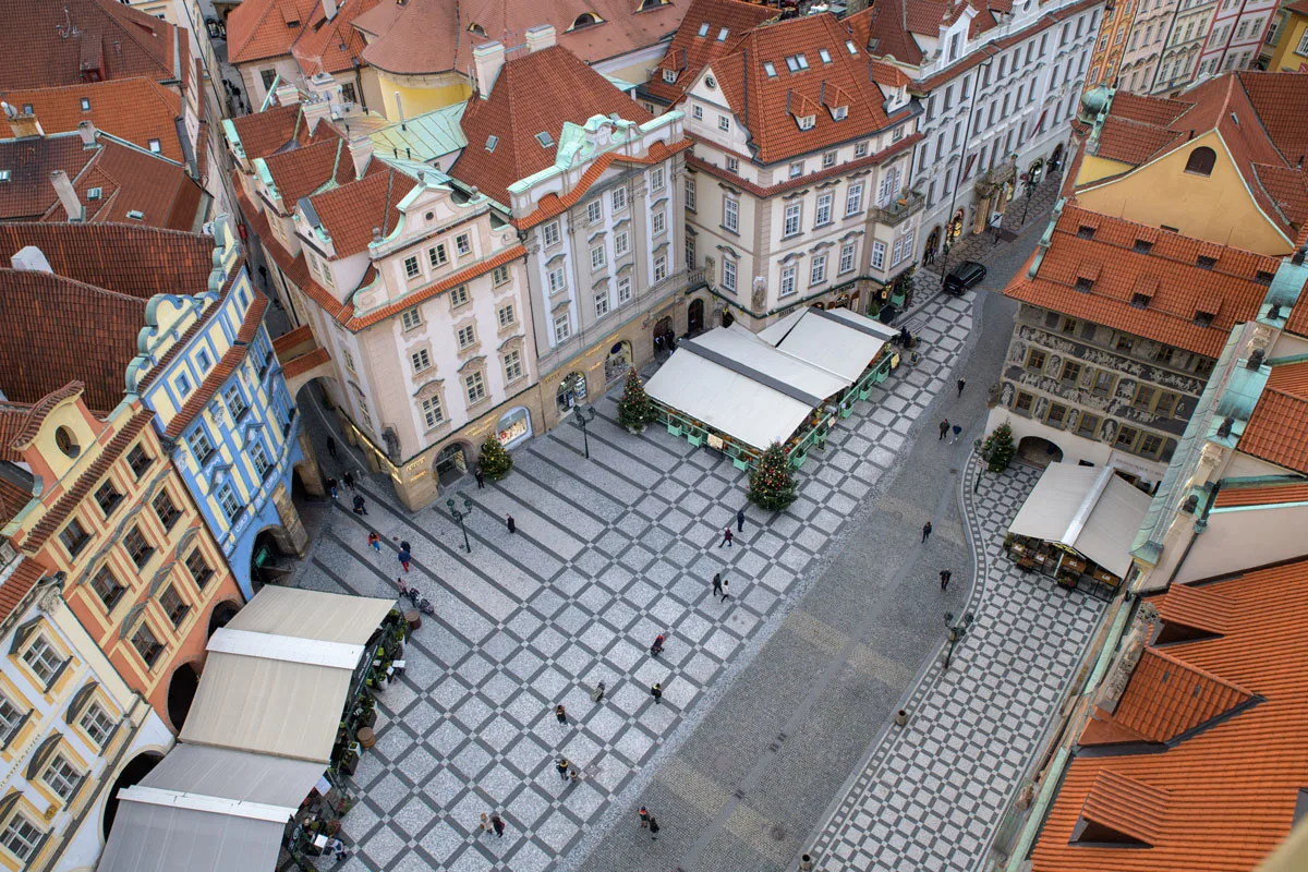 Looking down on the red roofs of the colourful buildings in Prague. There is a square with restaurants and aChristmas tree.  