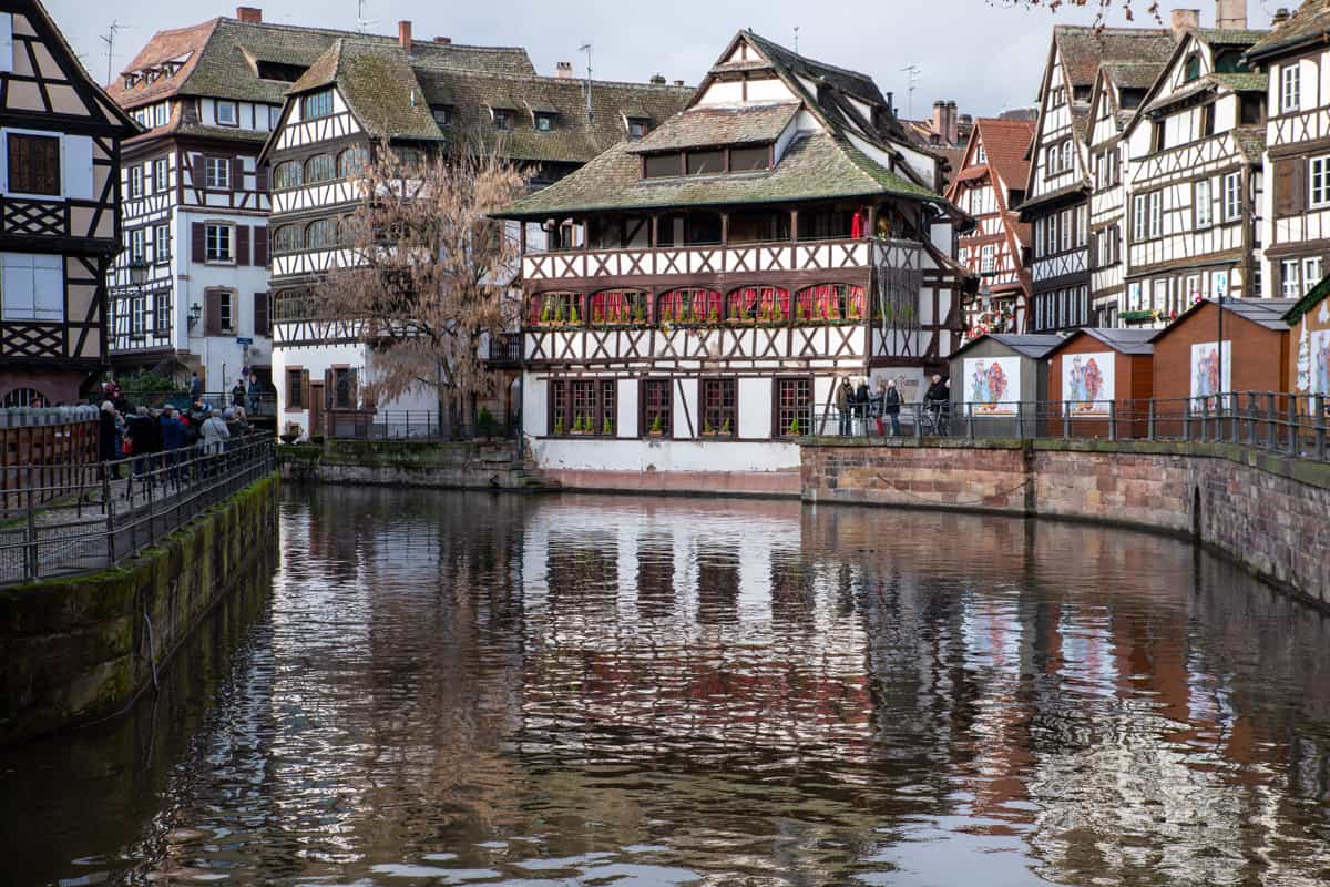 Traditional white and wooden houses line a river in the town of Strasbourg in France. The houses are reflecting in the water. 