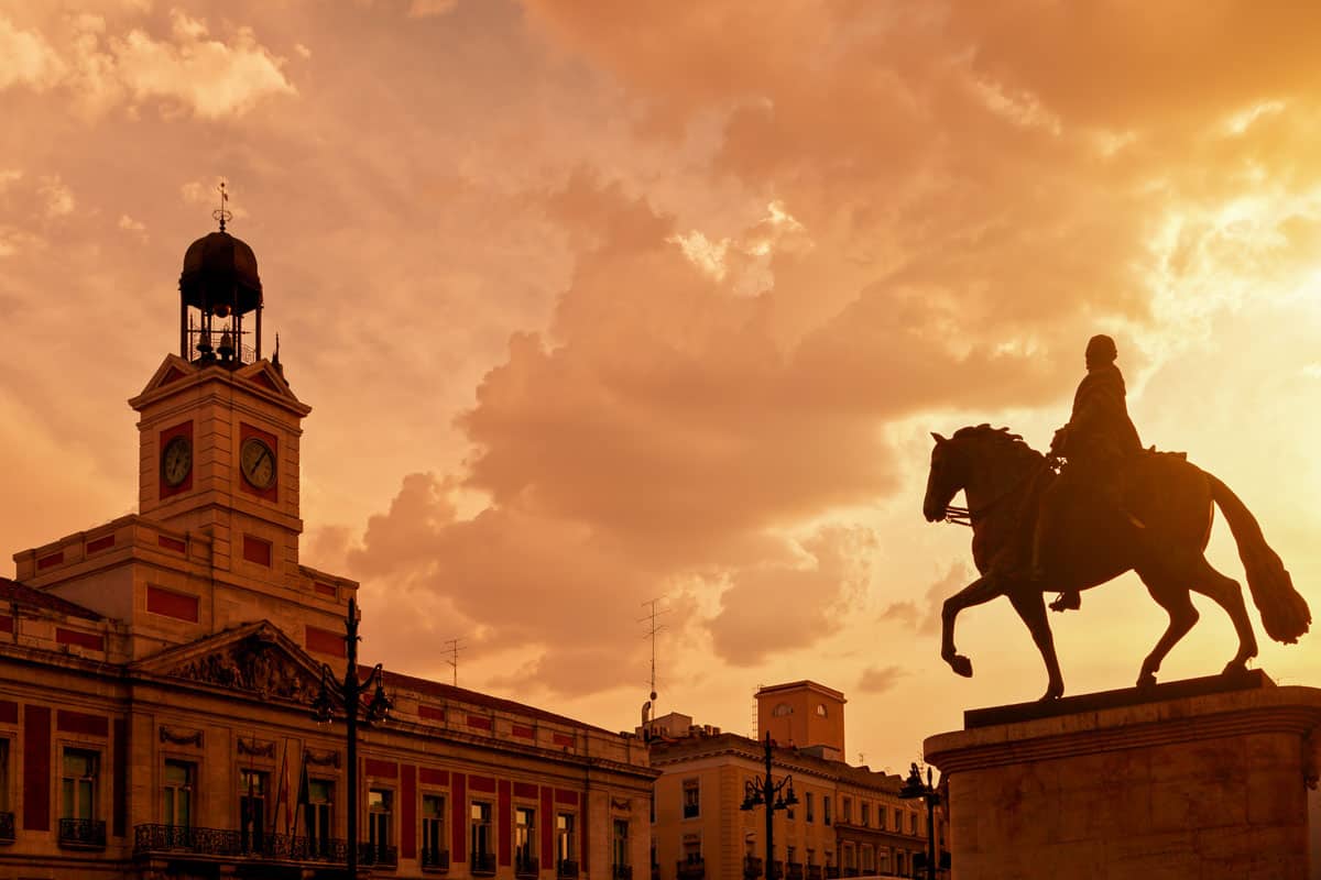 Silhouette of a horse statue and domed building in Puerta del Sol Plaza in Madrid against the red sunset sky.
