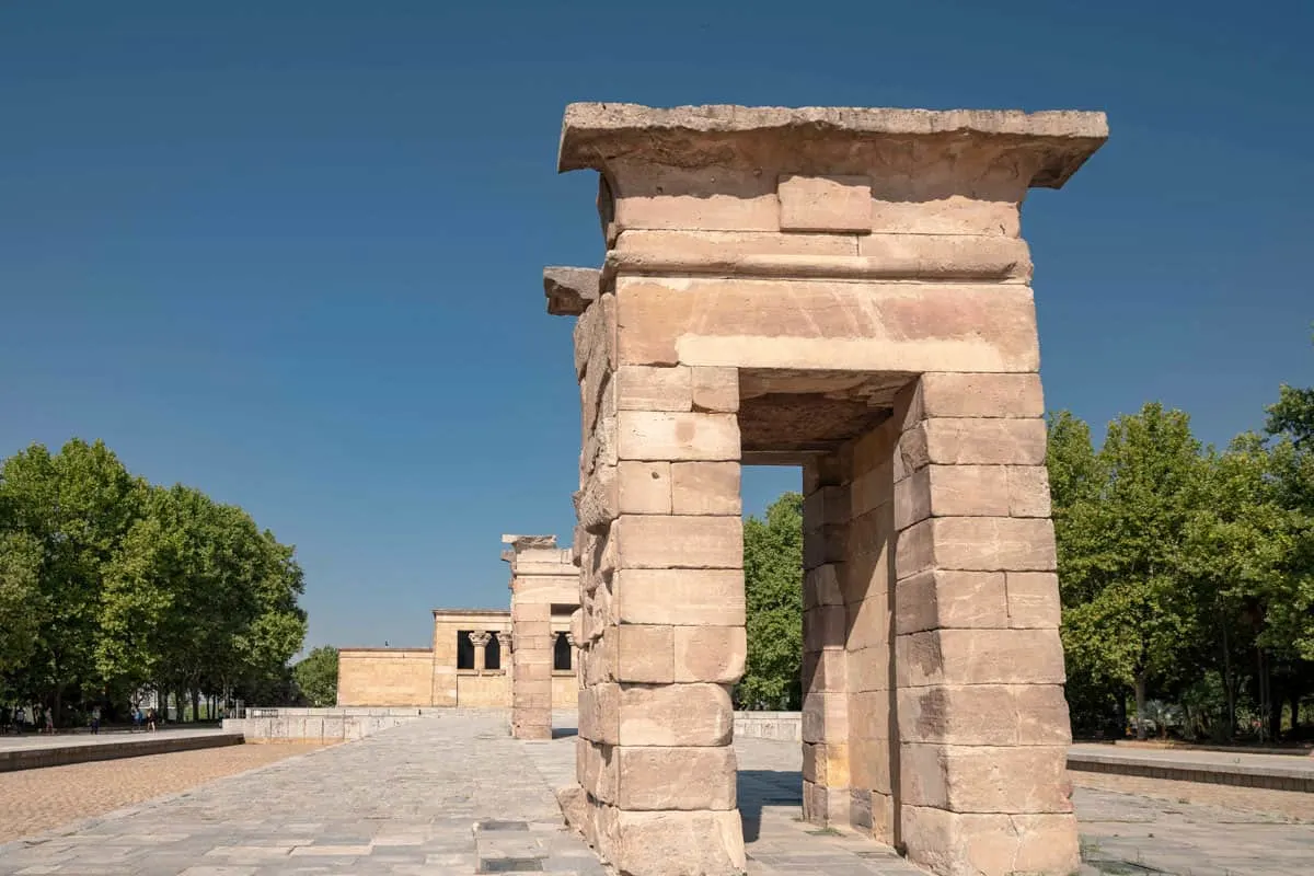 Stone structures of an ancient temple. There are trees to the side with a blue sky. 