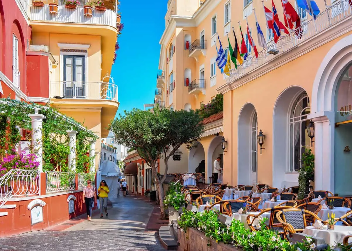 Tourists walking dow a colourful street with Italian cafe's in Capri Town.