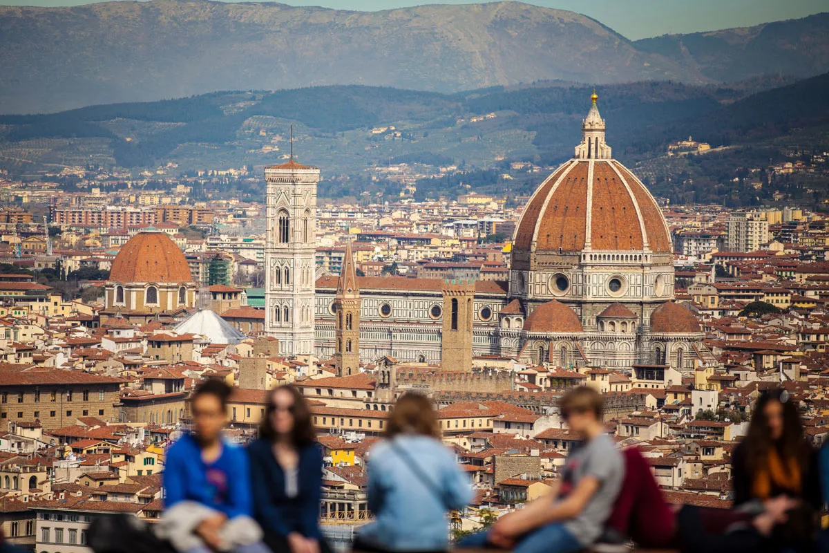 Tourists admiring the view over Florence from Piazzale Michelangelo. The city scape is in focus and the tourists are out of focus. 