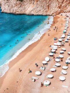 Umbrellas in neat rows on a yellow sand beach with incredibly beautiful turquoise water at Kaputas beach in Turkey.