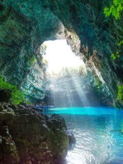 Light shines through a hole in the roof of a cave onto clear blue water. Row boats are in the light.