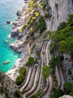 Looking down at a tightly winding road on the coast of clear water.
